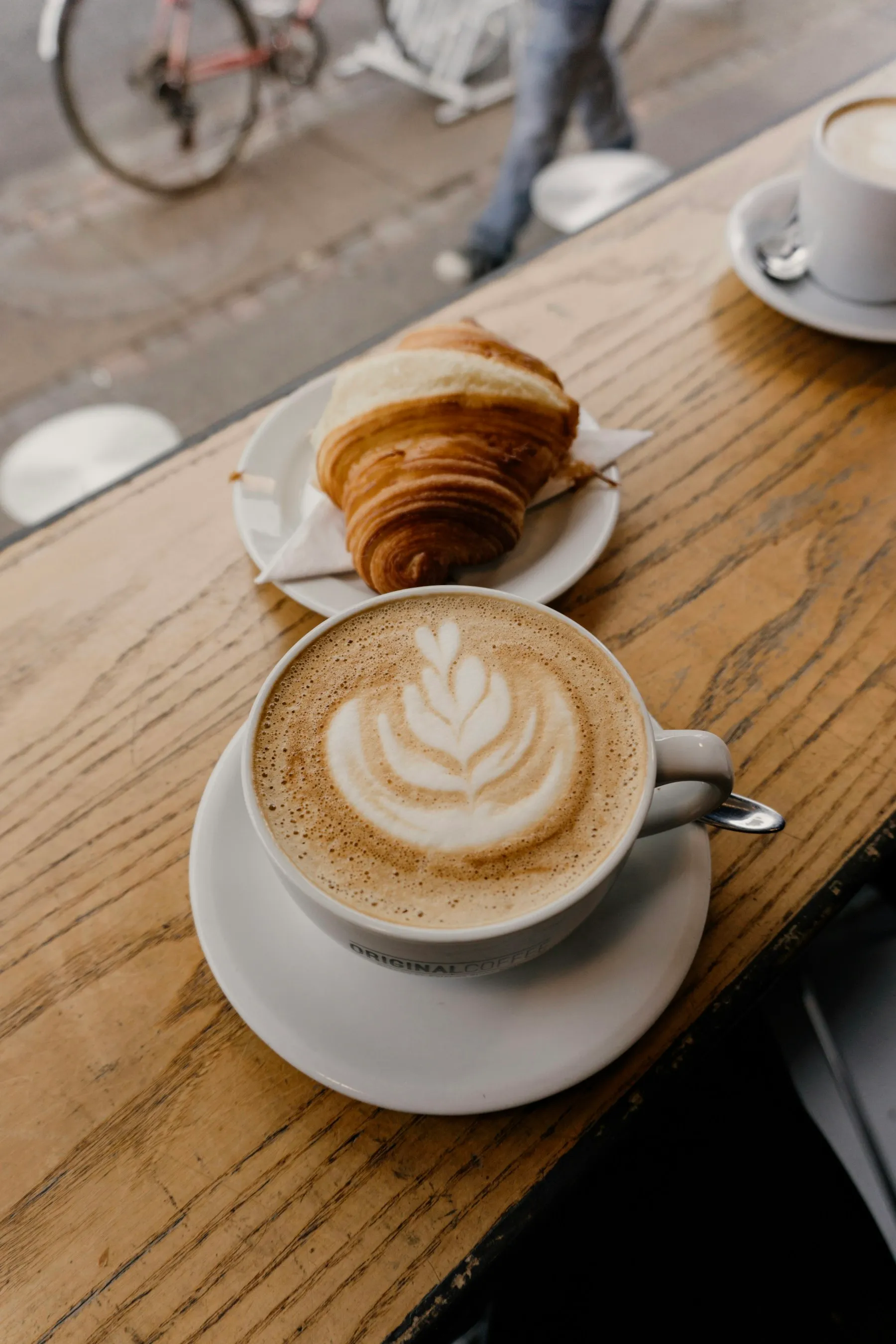 Ahşap masada yan yana duran bir cappuccino ve kruvasan