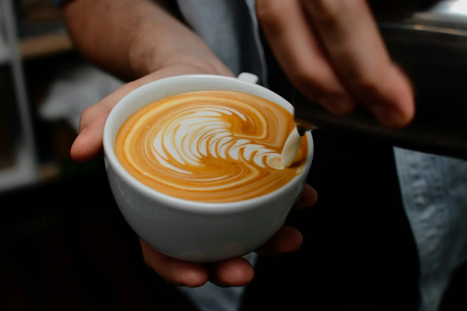 İki elin arasında tutulan, desenli köpüğüyle bir latte